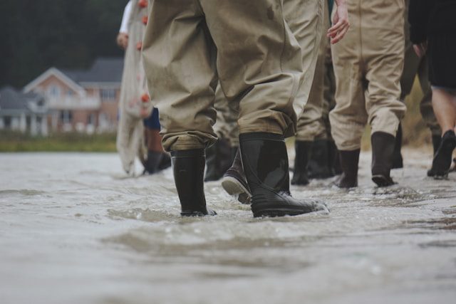A group of people wearing rain boots on a flooded street.