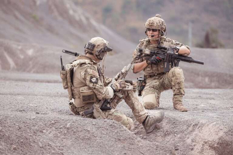 Two soldiers sitting in a rocky area with tactical gear.