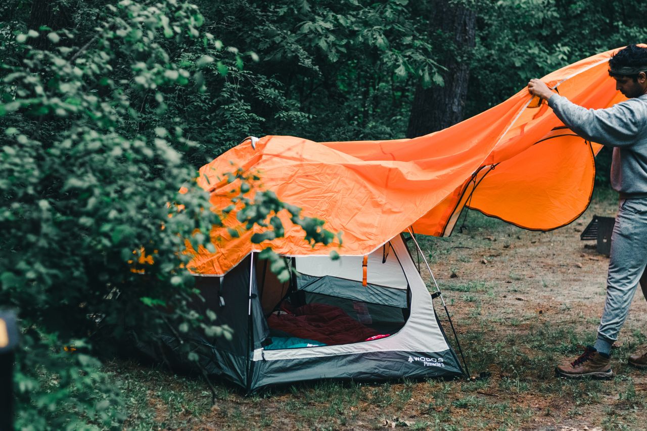 Person assembling a multi-part tent in the woods.