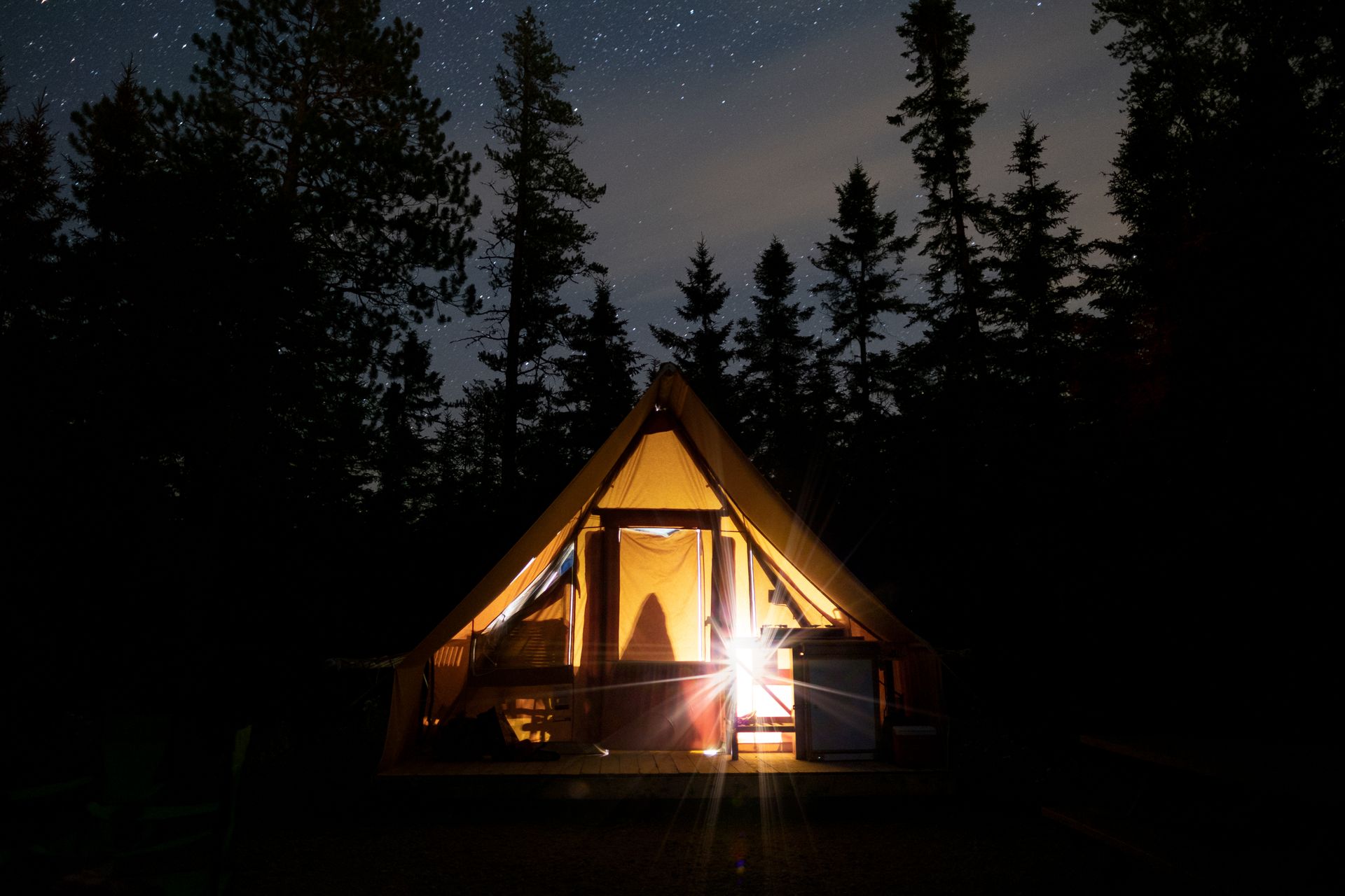 A tent with a light and gear set up in the wilderness.